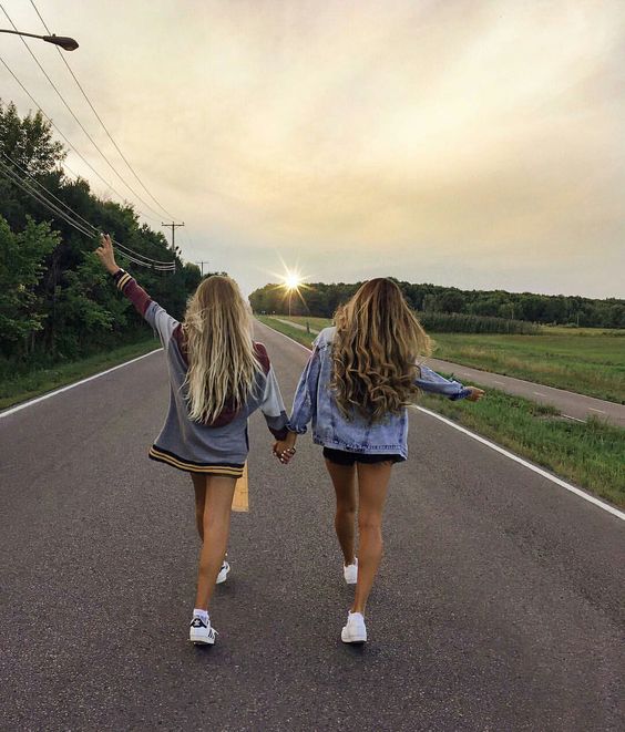 Two best friends walking down an empty road facing away from viewer. 