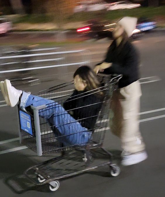 One girl pushing another girl sitting in a shopping cart